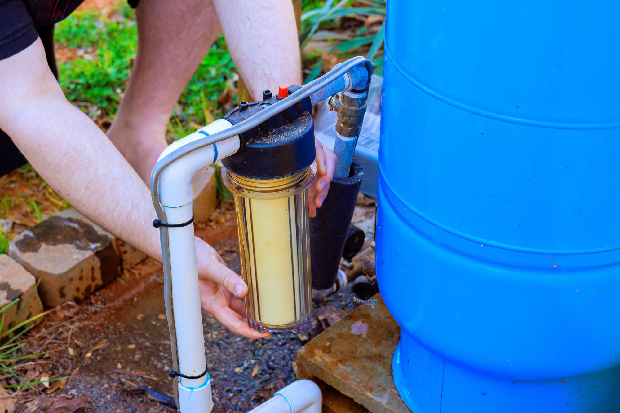 Working on a water filtration system with a yellow filter in a backyard on a sunny day
